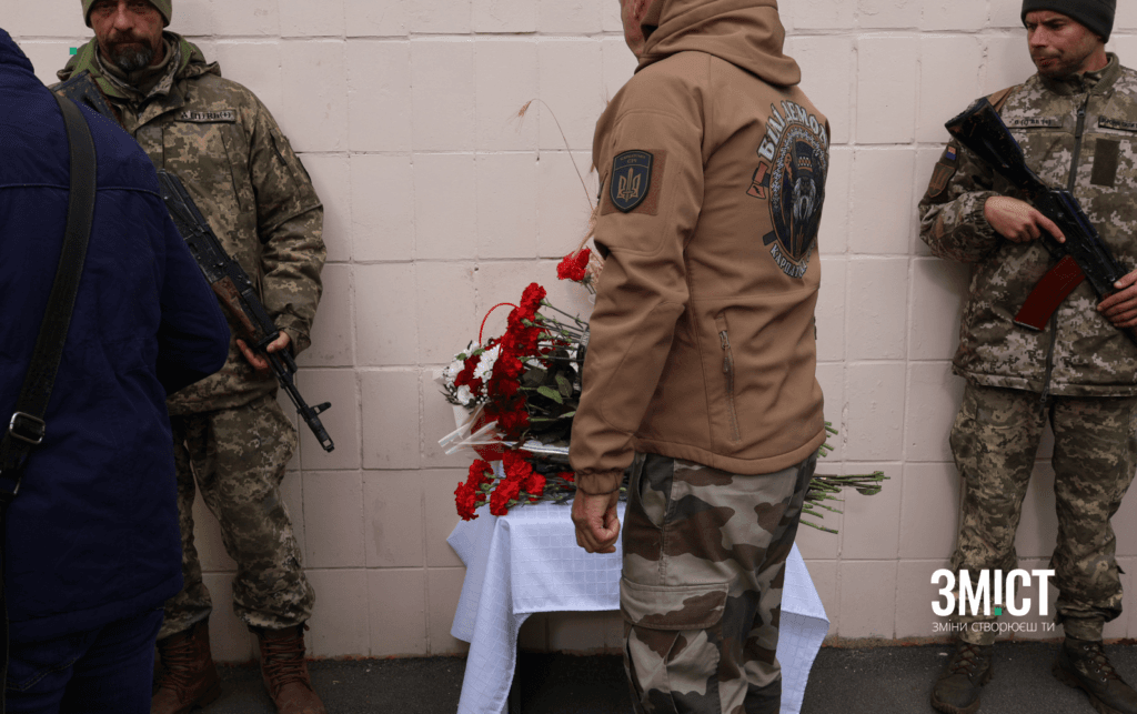 Побратим загиблого воїна кладе квіти до меморіальної дошки.